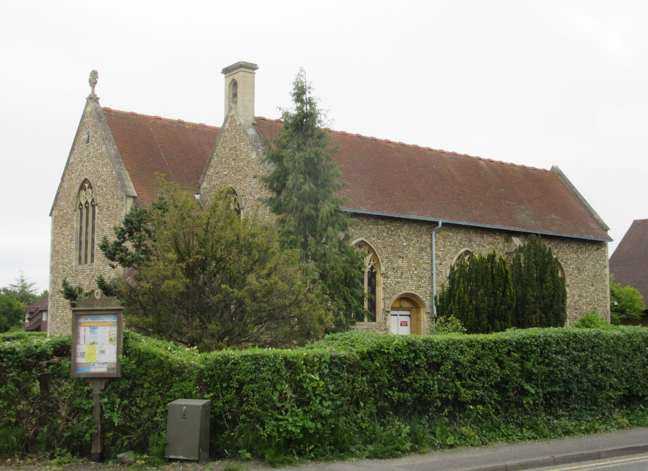 Historic stone church with arched windows surrounded by greenery and hedges.