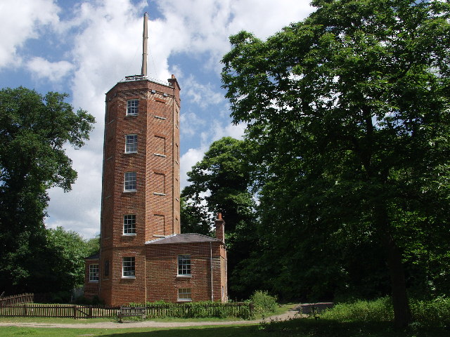 Historic brick tower surrounded by lush green trees under a partly cloudy blue sky.