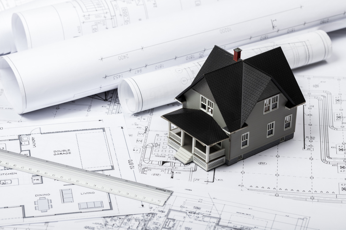 Model house on architectural blueprints, surrounded by rolled plans and a ruler, symbolizing home design planning.